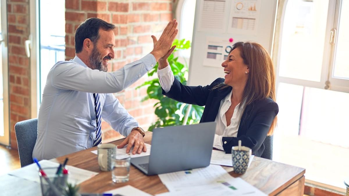 Zwei Kolleginnen und Kollegen klatschen im Büro lachend ab